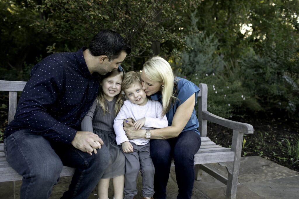 Smiling family of four sitting together on a garden bench, surrounded by colorful blooms