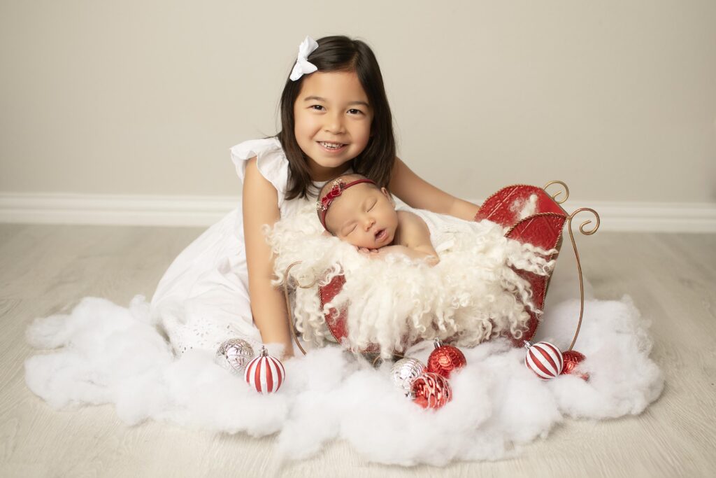 Big sister and newborn girl with christmas sleigh