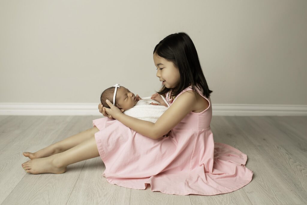 Big sister protectively wrapping her arms around her newborn sister