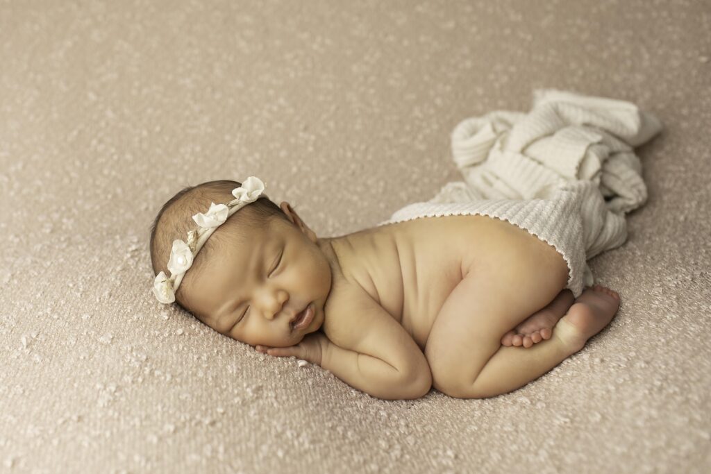 Close-up of newborn girl sleeping soundly on a mauve blanket, with a tiny headband adorned with flowers