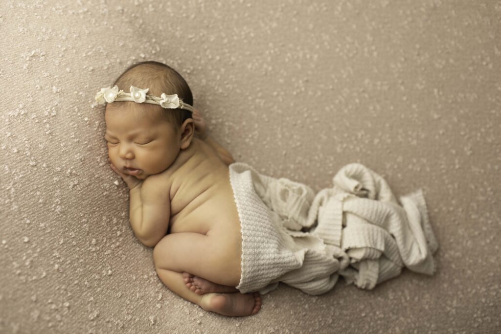 Simple, classic pose of a newborn girl resting her chin on her hands atop a mauve blanket