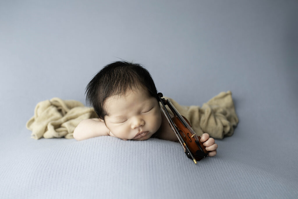 newborn holding a mini violin, gently resting it on his shoulder