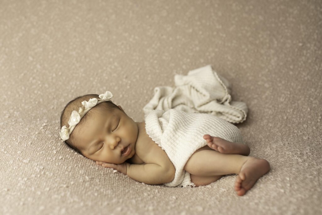 Newborn girl peacefully sleeping on a mauve blanket, wearing a delicate headband