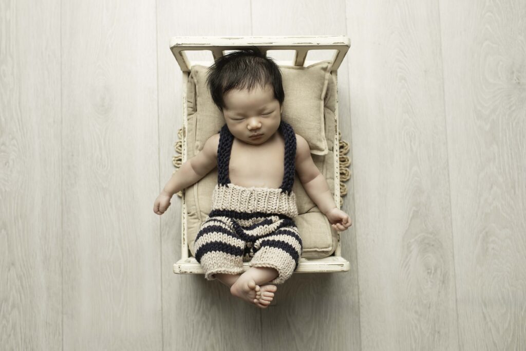 Newborn boy lying on a soft bed, wrapped in a neutral-toned blanket, resting his head on a small pillow