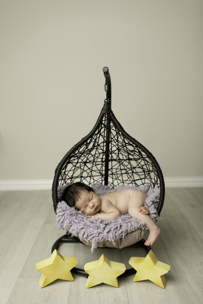 Newborn boy peacefully sleeping in a hanging basket, gently swaddled in a soft blanket, with a rustic, cozy backdrop