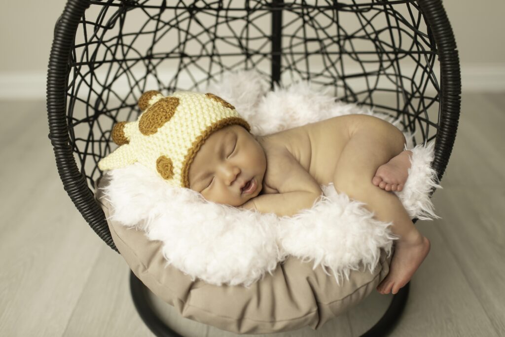 Newborn girl curled up in a hanging basket, surrounded by soft textures and warm tones