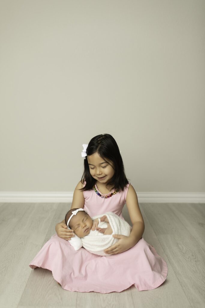 Big sister looking down lovingly at her sleeping newborn sister