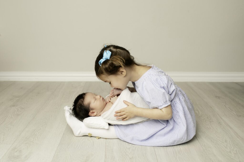 Big sister gently kissing her newborn baby brother on the toe, showing a tender moment of love.