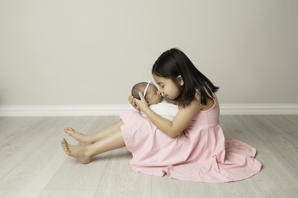 Big sister resting her head on her newborn sister’s tiny body