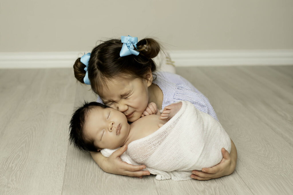 Big sister lovingly staring at her newborn baby brother, gazing at him with wonder and affection.