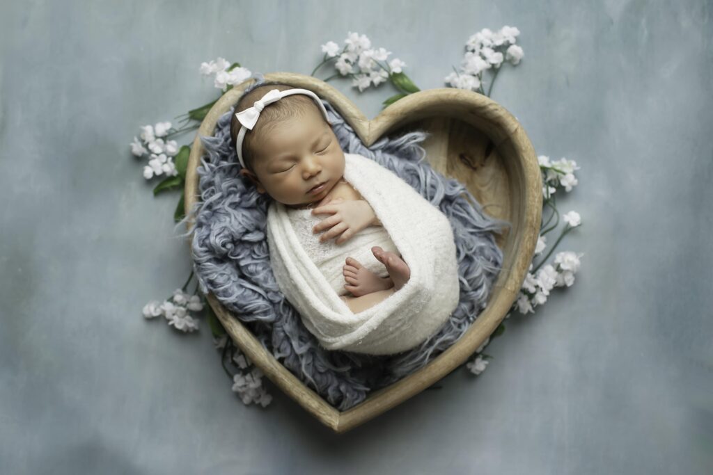 Newborn girl nestled inside a heart-shaped prop, swaddled in neutral tones