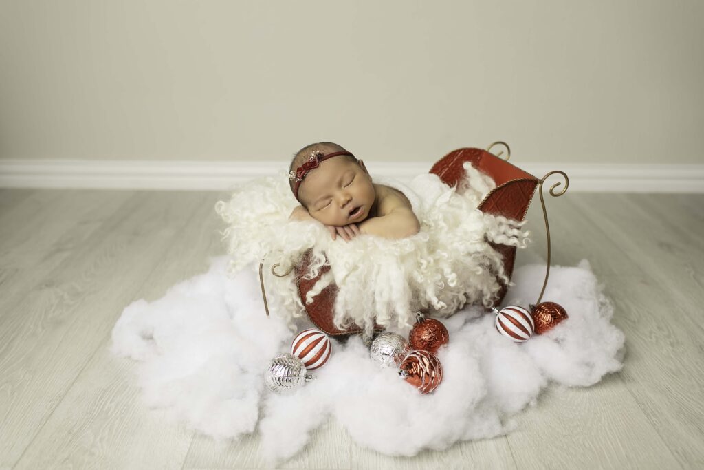 Cozy pose of a newborn girl sleeping in a red sleigh, wrapped in soft blankets