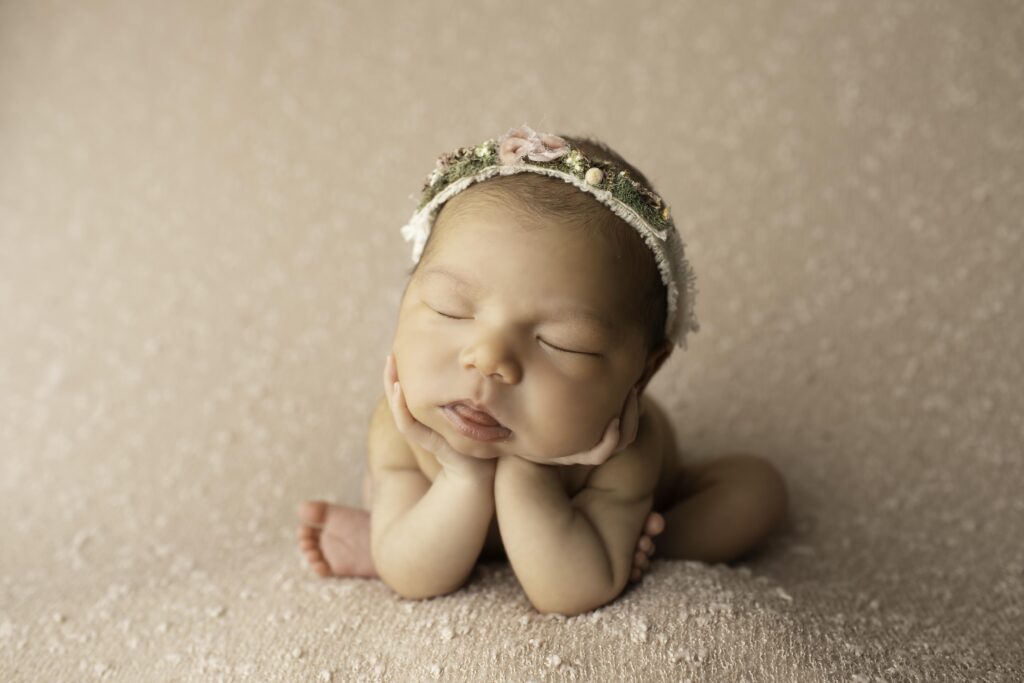 Newborn girl resting her hands under her chin, lying on a mauve blanket with a delicate headband