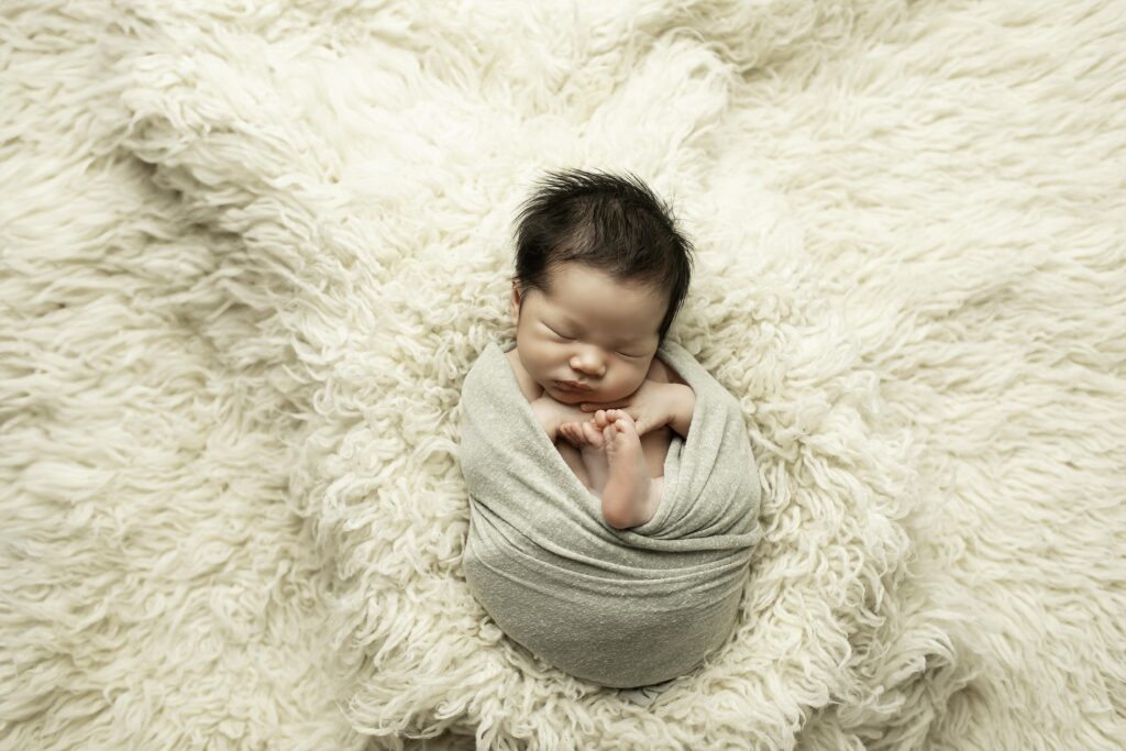 Newborn boy peacefully sleeping in a soft, cozy basket, surrounded by textured blankets and neutral tones