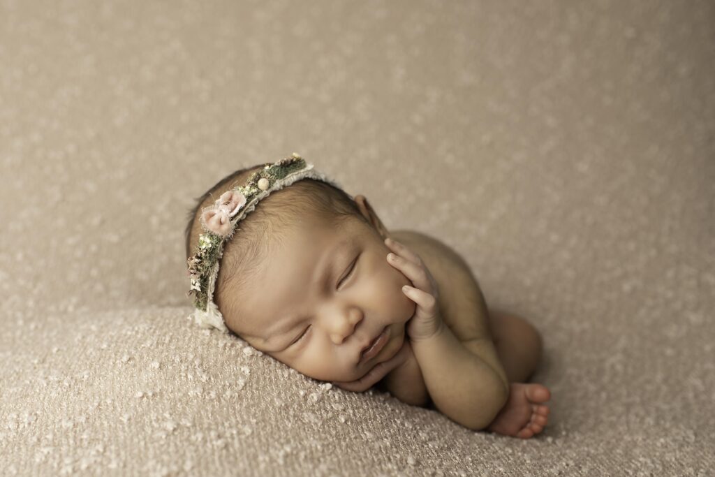 Side profile of a sleeping newborn girl on a mauve blanket, headband adding a sweet touch