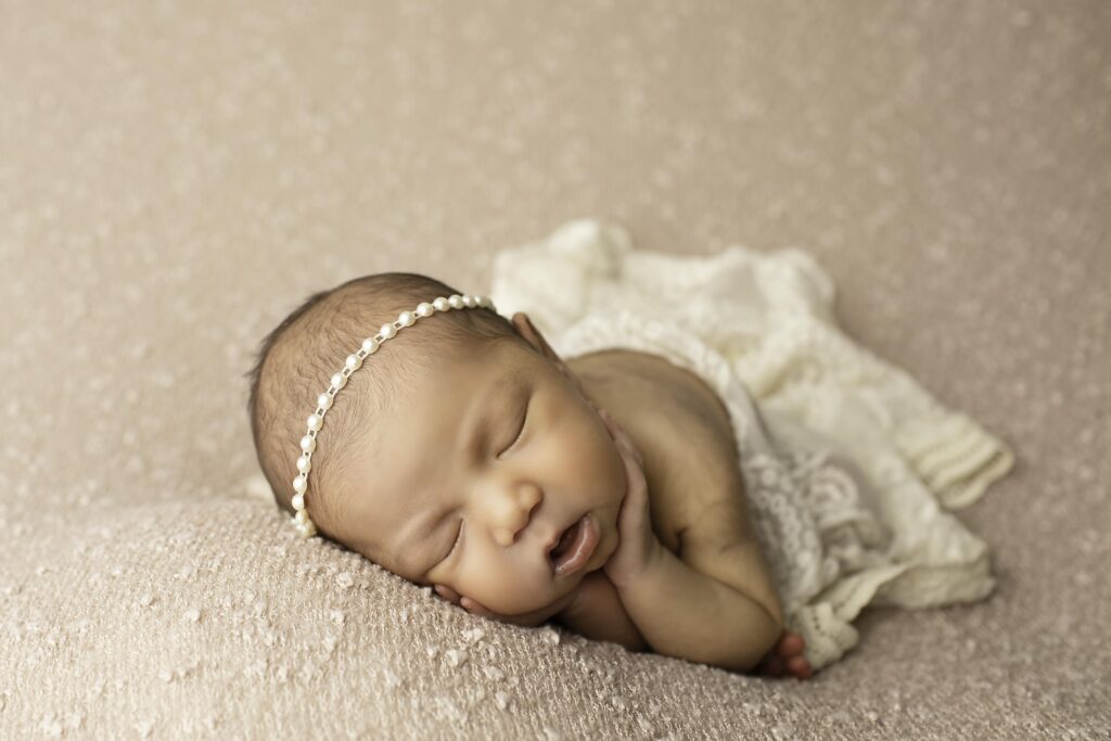 Minimalistic pose of newborn girl wrapped in a mauve swaddle, tiny headband resting on her forehead