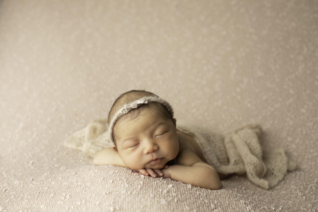 Newborn girl curled up on a mauve blanket, soft headband framing her peaceful face